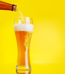 A frothy glass of fresh beer against a bright yellow background