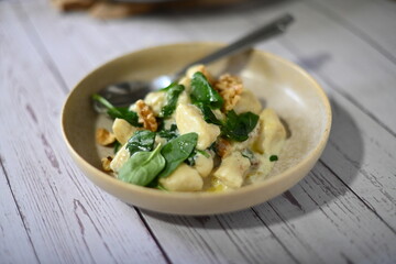 Close-up view of potato gnocchi served with a creamy blue cheese sauce and walnuts on a white plate. A rich and flavorful dish combining soft, pillowy gnocchi with the bold taste of blue cheese 