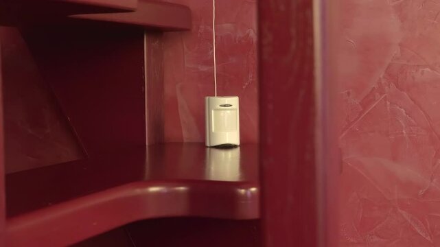 In the house on the red wooden staircase there is a white motion sensor of signaling, on which a blue LED lights up, indicating the detection of movement and possible illegal entry into the home