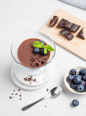 Chocolate pudding in a glass with fresh blueberries and mint on a light background