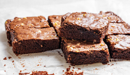 Chocolate brownie with nuts cut into pieces on baking paper close-up with morning light.