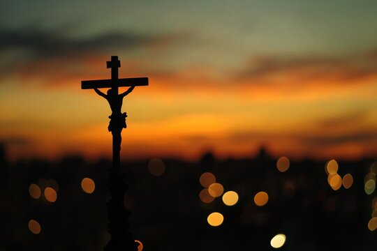 Silhouette of Jesus on the cross against sunset sky dark background with bokeh effect