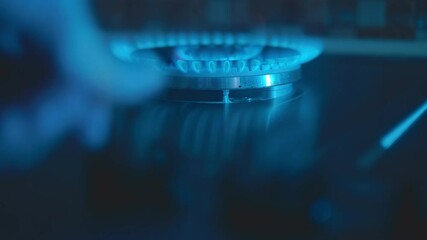 In the kitchen, in the dark on the stove, the hand ignites the gas on a large and powerful burner consisting of two rings and then turns off the gas. Closeup. Shot in motion. Follow focus