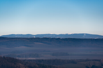 Distant view of the Jeseniky Mountains with Praded peak rising above the horizon. The vast landscape showcases rolling hills, deep forests, and the beauty of Czech nature