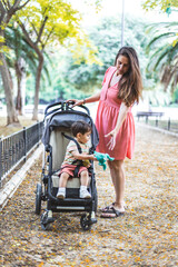 A mother with her son sitting on a stroller in the park interact with a toy