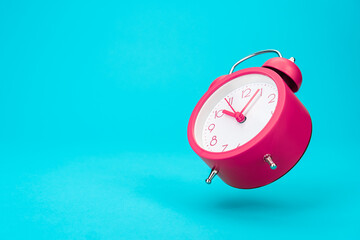 Pink alarm clock in the air over turquoise blue background with copy space. Minimalist photo of jumping and ringing alarm clock. Time management concept.