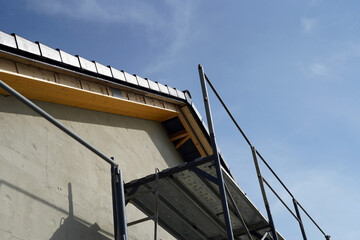 A view of a house under construction outside. We can see the unfinished facade, the edge of the roof, and the scaffolding erected.