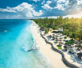 Aerial view of the sailboat on blue sea, empty white sandy beach, umbrellas at sunset. Summer in...