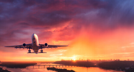 Airplane is flying in colorful sky over city at sunset. Landscape with passenger airplane, skyline,...
