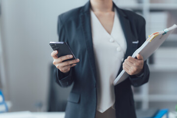 Business Professional with Smartphone and Documents: A cropped image of a businesswoman holding a smartphone and documents in her hands, demonstrating modern corporate communication.