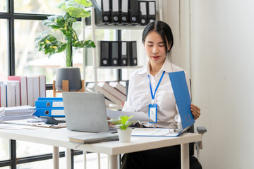 Focused Professional Woman: A young businesswoman sits at her desk, meticulously reviewing...