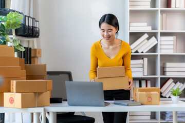 Online Business Owner:  A young, smiling woman entrepreneur confidently handles packages in her...