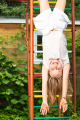 Obraz premium Happy blonde child hanging from playground ladder in sunny outdoor setting