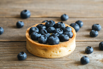 Homemade mini tart with blueberries and whipped cream on a wooden background, close up.