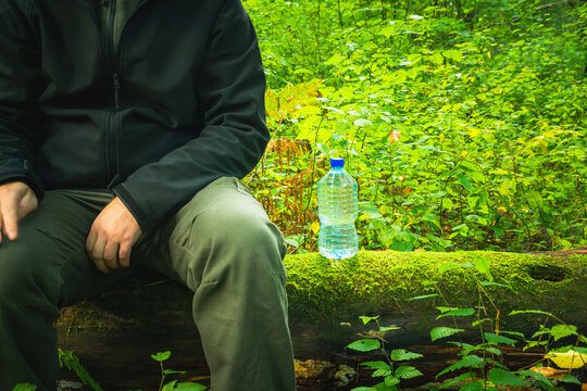 A man sitting on a tree trunk and a bottle of water
