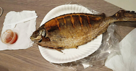 Photo of appetizing fried dorado fish with head and tail. Plastic jar of red spicy sauce. Traditional Thai street food. Delicious exotic groceries. Yummy fast lunch. Popular seafood. Beach breakfast.