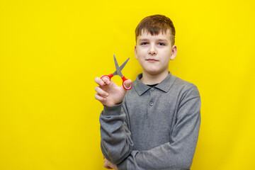 boy in gray sweater holds scissors in hand on yellow background