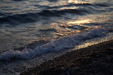A sea wave at dusk. Water reaching the shore of a pebble beach in the afternoon sun. With space to copy. High quality photo