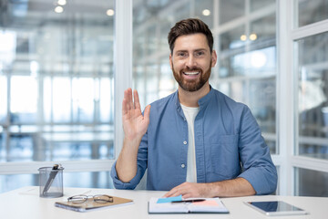 Web camera view, man joyfully looking at camera waving hand, greeting gesture. Businessman at...