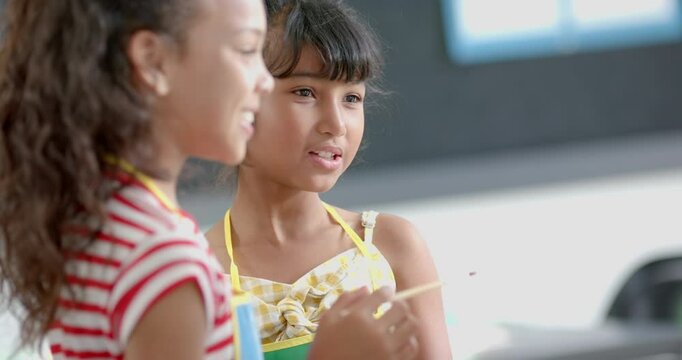 Two biracial girls talk in school classroom, one holding a pencil