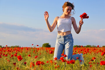 Beautiful young girl is jumping in flower poppy field, picking flowers and enjoying. Beauty in nature, rural landscape, lots of red flowers in meadow. Low angle view