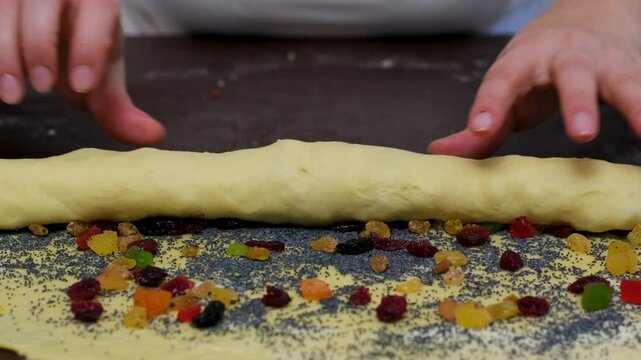 A woman prepares a cruffin with raisins and candied fruits. Rolls the dough cruffin. Tools and ingredients are laid out on the table.