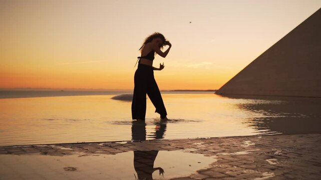 Woman dancing in water at sunset. Sensual barefoot dance. Girl in black performs a slow, seductive, freestyle contemporary dance, expressing freedom