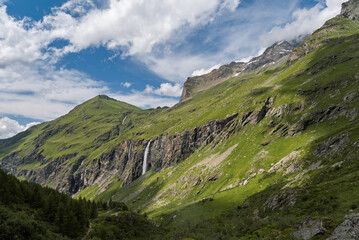 Fototapeta premium Witness the breathtaking beauty of the French Alps with this stunning photograph taken in Savoie. The image captures a dramatic mountainous landscape featuring lush green slopes and rugged rocky cliff