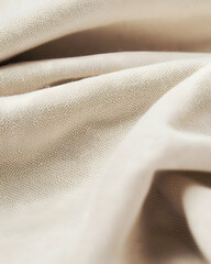 Close-up shot of a soft beige fabric. The fabric has a subtle texture with a centered fold, creating depth and dimension. 