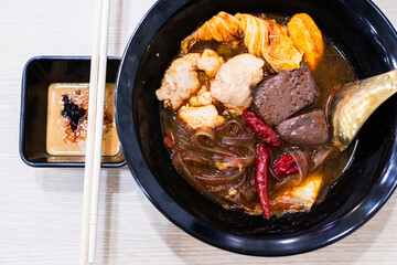 Mala hot pot soup served in a black bowl, consisting of sweet potato noodles, chicken blood and tender marinated pork.
