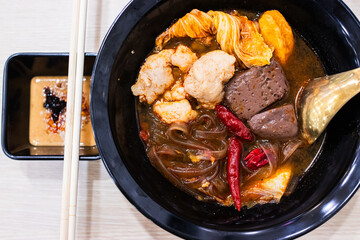 Mala hot pot soup served in a black bowl, consisting of sweet potato noodles, chicken blood and tender marinated pork.