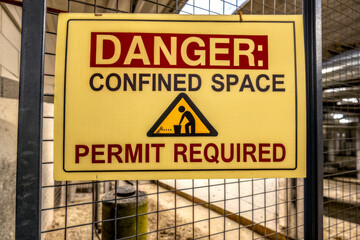 A safety sign warning about the dangers of confined spaces and indicating that a permit is required for entry.