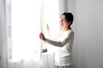 カーテンを開け日光を浴びるアジア人女性
