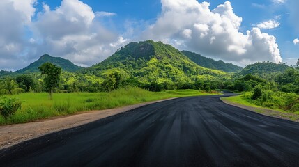 A wide, empty road square contrasts beautifully with the towering green mountains, set against a backdrop of blue skies and scattered clouds.