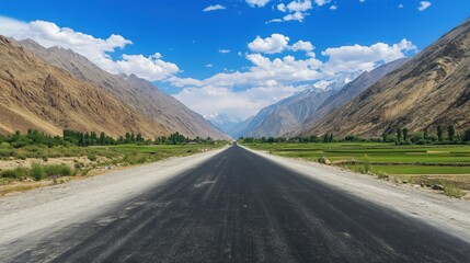 Naklejka premium A long, empty road leads through rolling green hills, with towering mountains in the distance, under a bright and clear blue sky.