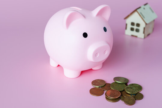 A piggy bank in the form of a pink pig, small coins and a mock-up of the house. The concept of savings and investments for the purchase of real estate.