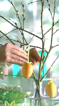 A young woman serves a festive Easter table with a yellow bunny decoration. Sunlight fills the cozy room, highlighting elegant tableware, pastel colors, and holiday decor. A warm family moment full of
