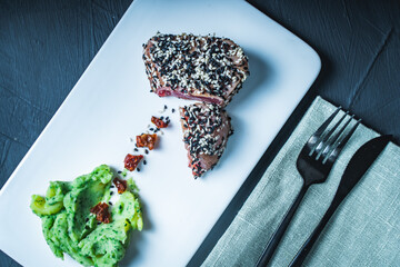 Raw tuna slices with black and white sesame seeds on a black background.