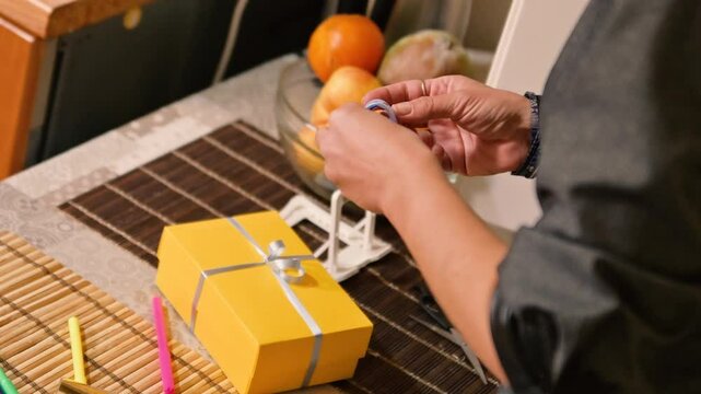 A woman wraps a gift in a yellow gift box. The scene focuses on the act of gift-wrapping, showcasing the care and attention to detail involved in preparing a present. The woman might be tying a ribbon