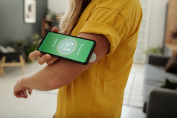 Closeup of unrecognizable woman putting smartphone to CGM device on arm while monitoring glucose levels for diabetes care copy space