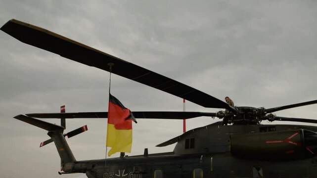 German flag and the helicopter Sikorsky CH-53GS which participates at Bucharest Air Show BIAS 2024. A pilot sits on the helicopter propellers and watches the show.