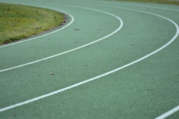 Green running track curve with white lines and green grass in the sides.