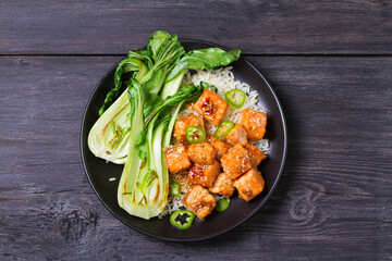 Delicious salmon with salad, rice and sesame seeds on black plate and black wooden background. View from above, top studio shot