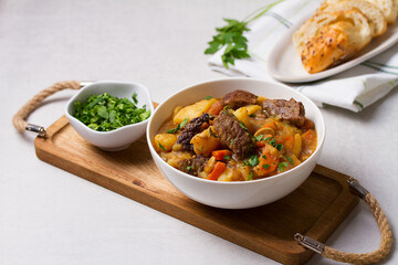 Delicious beef stew with vegetables in a white bowl on white background