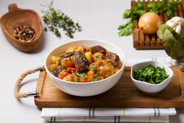 Delicious beef stew with vegetables in a white bowl on white background