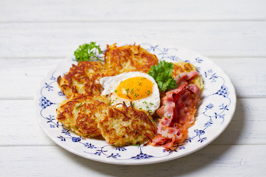 Hash browns with fried egg and bacon on white plate and white wooden background