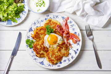 Hash browns with fried egg and bacon on white plate and white wooden background. View from above, top view