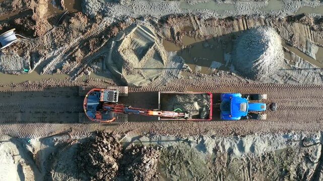 Digger crane filling loading cart during groundworks for housing development
