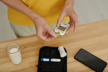 Top view closeup of female hands holding glucose meter while doing regular blood sugar checkup for...