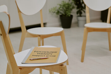 Subdued therapy setting with several empty wooden chairs arranged in circle around small table...